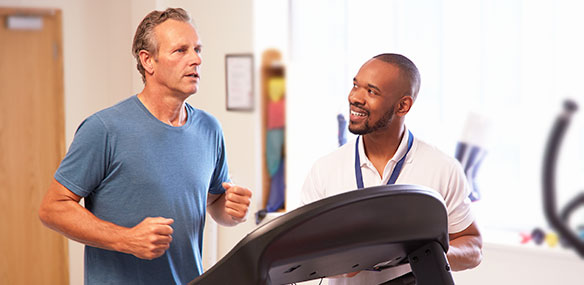Middle aged man exercising on treadmill with physical therapist