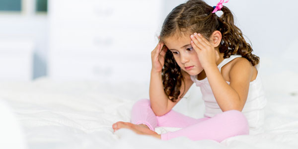 Young girl sitting on bed holding head