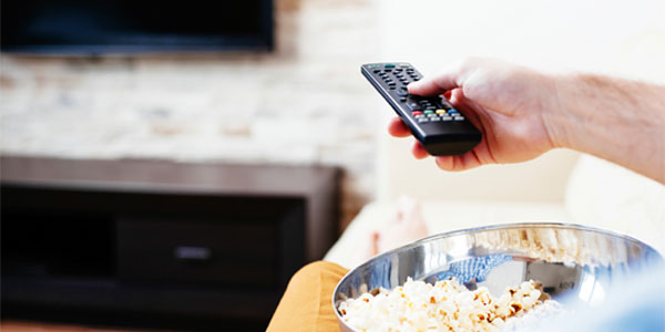 Close up of man sitting on couch with bowl of popcorn watching TV
