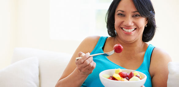Overweight African-American woman eating bowl of fruit