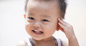 Asian toddler boy smiling with hand on head