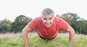 Older man doing push ups outside on the grass