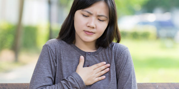 Young woman sitting on park bench with hand over heart