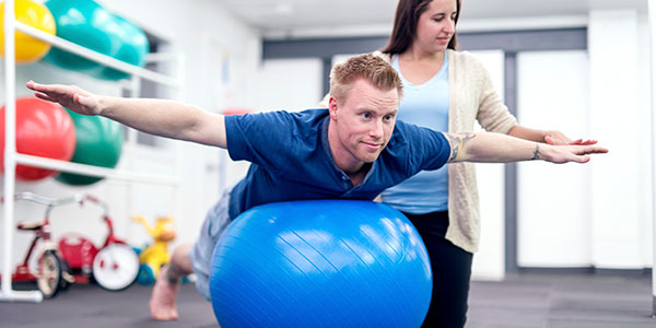 A therapist helps a man on a balance ball.