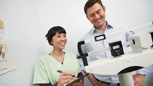 Asian nurse checking male patient's weight on scale