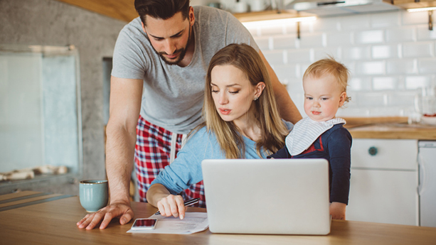 Couple holding a baby discussing while looking at a laptop