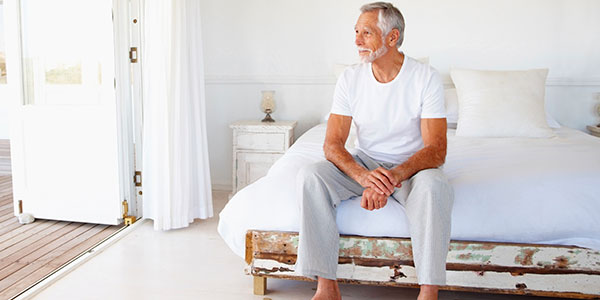 Older man sitting on corner of bed alone