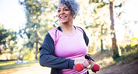 Smiling middle-aged woman walking outdoors holding hand weights