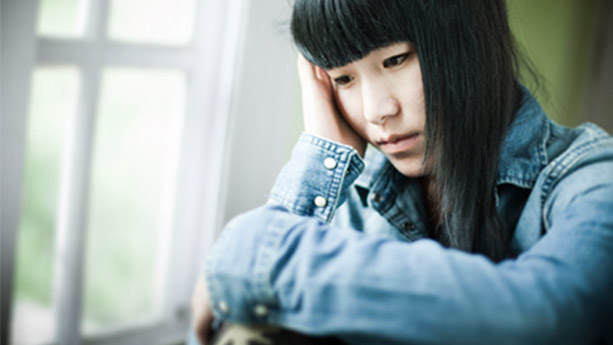 Female Asian teenager with sad expression looking out window
